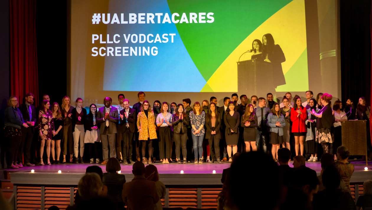 students pose on stage at the metro theatre with UAlbertaCares PLLC Vodcast Screening on the screen