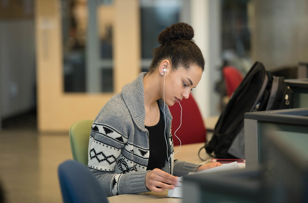 A student sits reading a textbook in a library computer lab