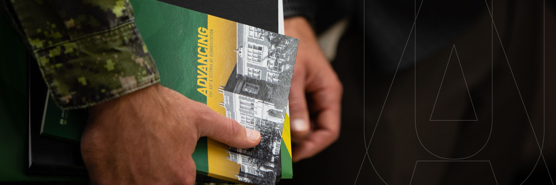 Close up image of hands holding a brochure. The arm is wearing an army jacket. 