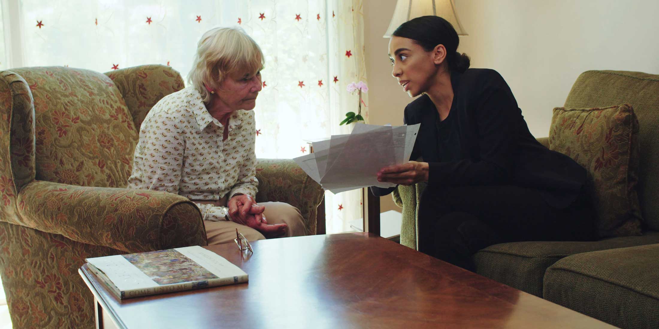 Young woman showing papers to older woman in a living room setting