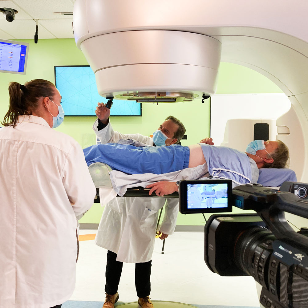Video camera recording a patient going in for a radiation scan with two technicians working