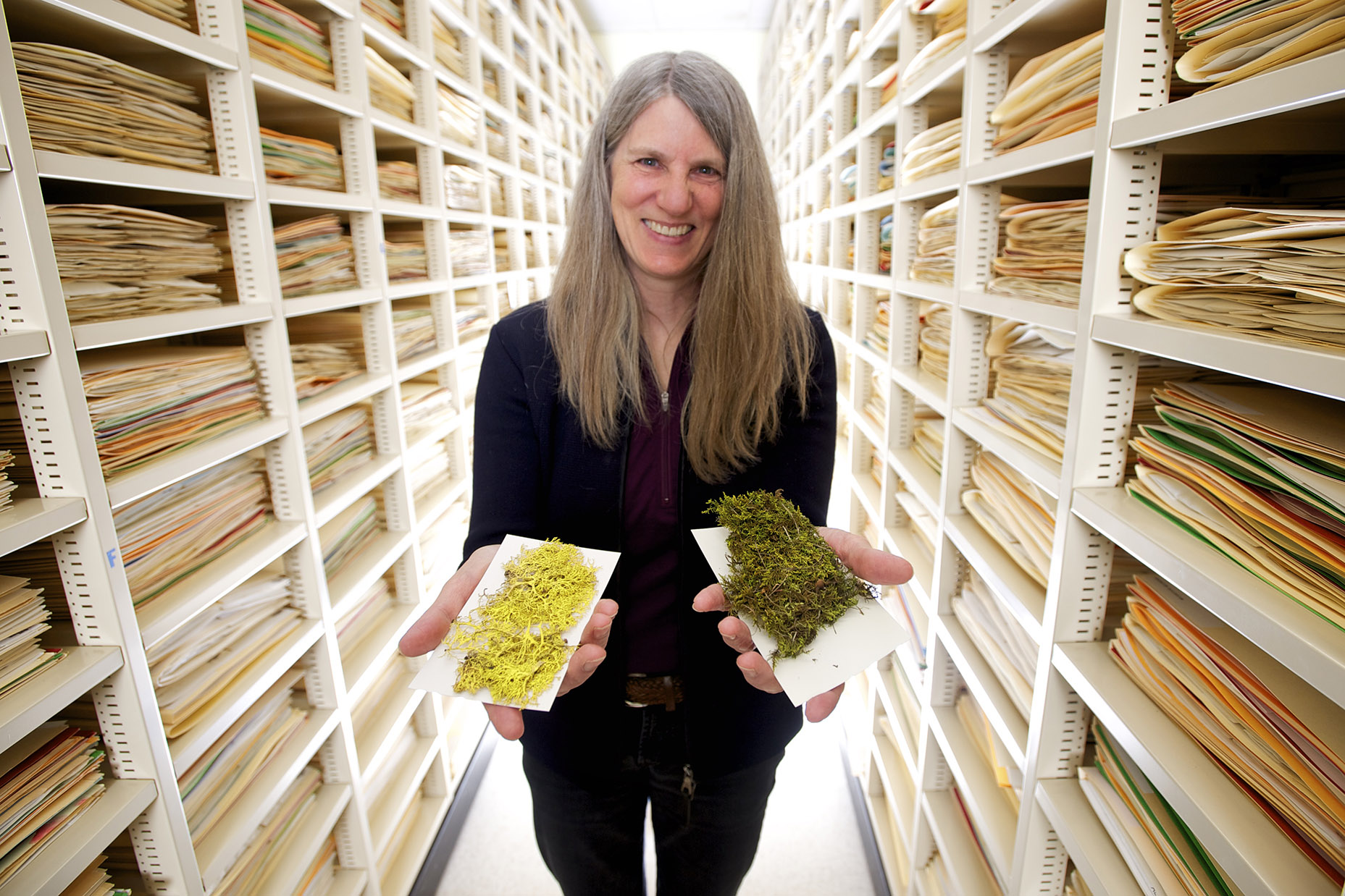 Catherine La Farge holding two specimens of moss placed on white cards in each hand.