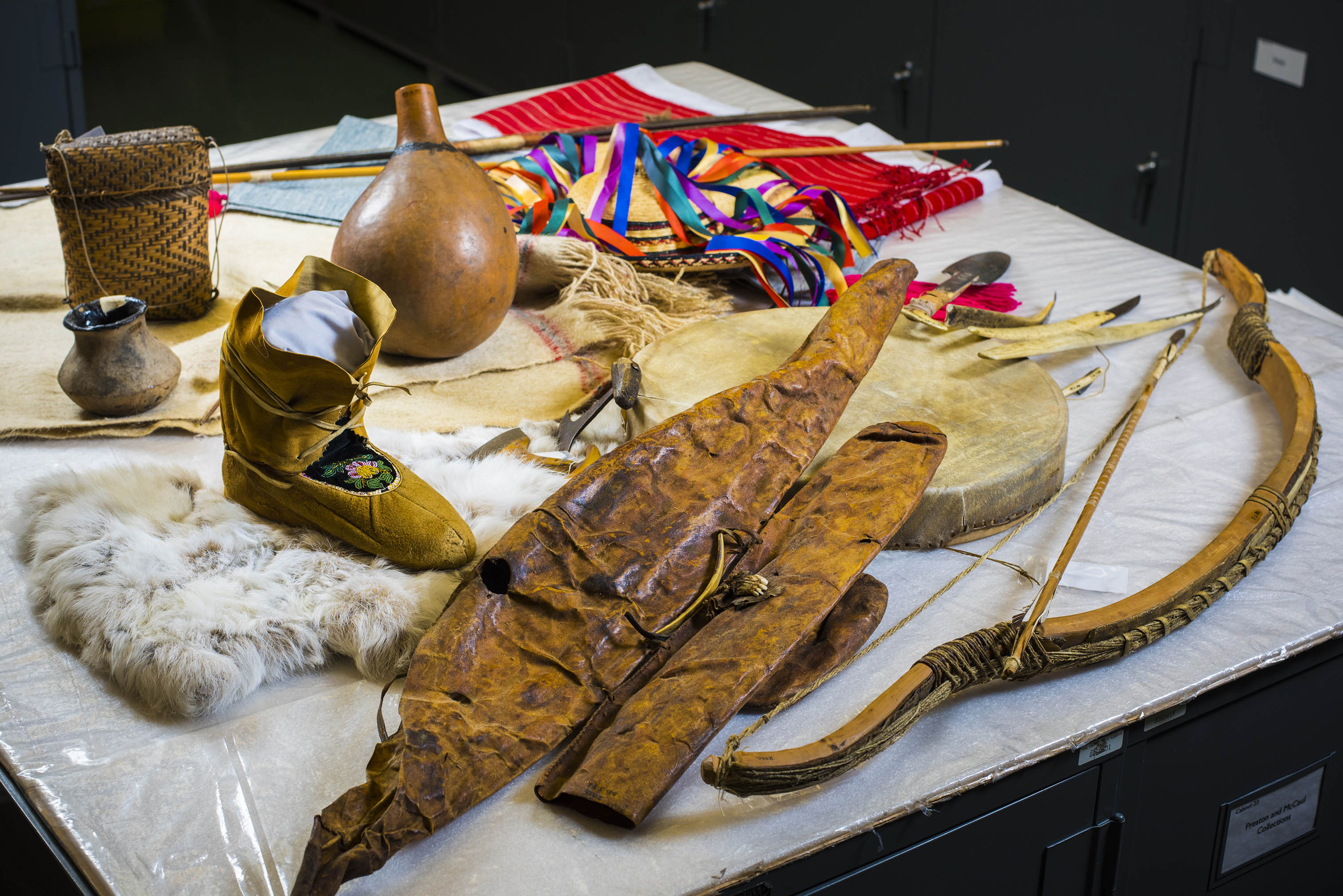 Artifacts on a covered table, including a moccassin, a piece of white fur, a bow, and two flattened, dried leather satchels.