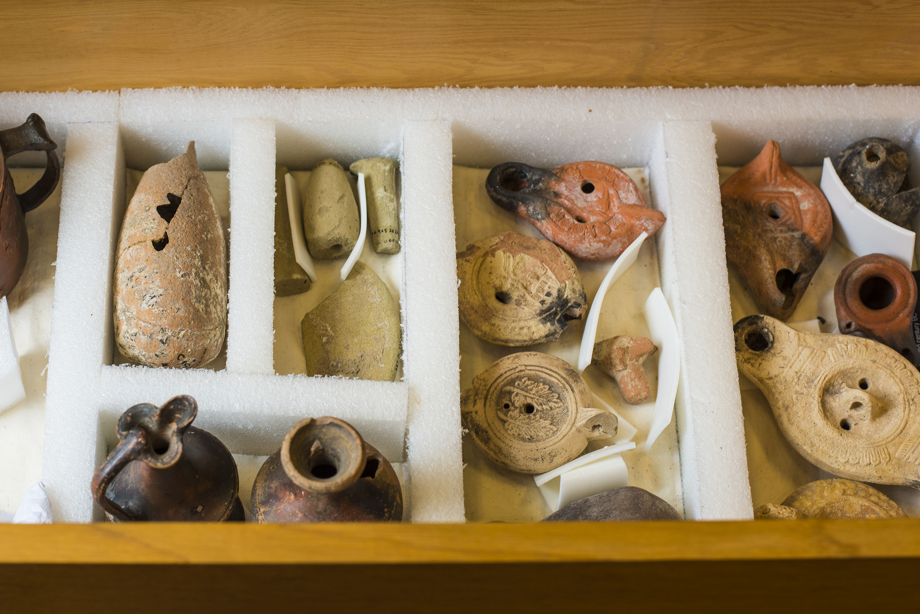 An assortment of small, fragmented clay artifacts, separated by walls of foam in a wooden box