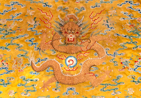 A golden dragon on a yellow silk textile, facing forward.