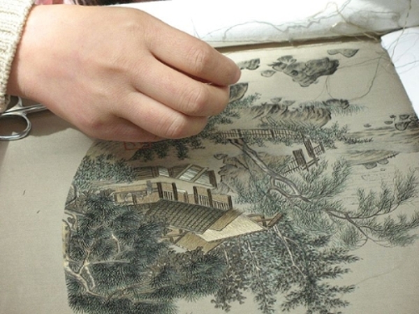 Overhead view of an individual embroidering a detailed outdoor landscape