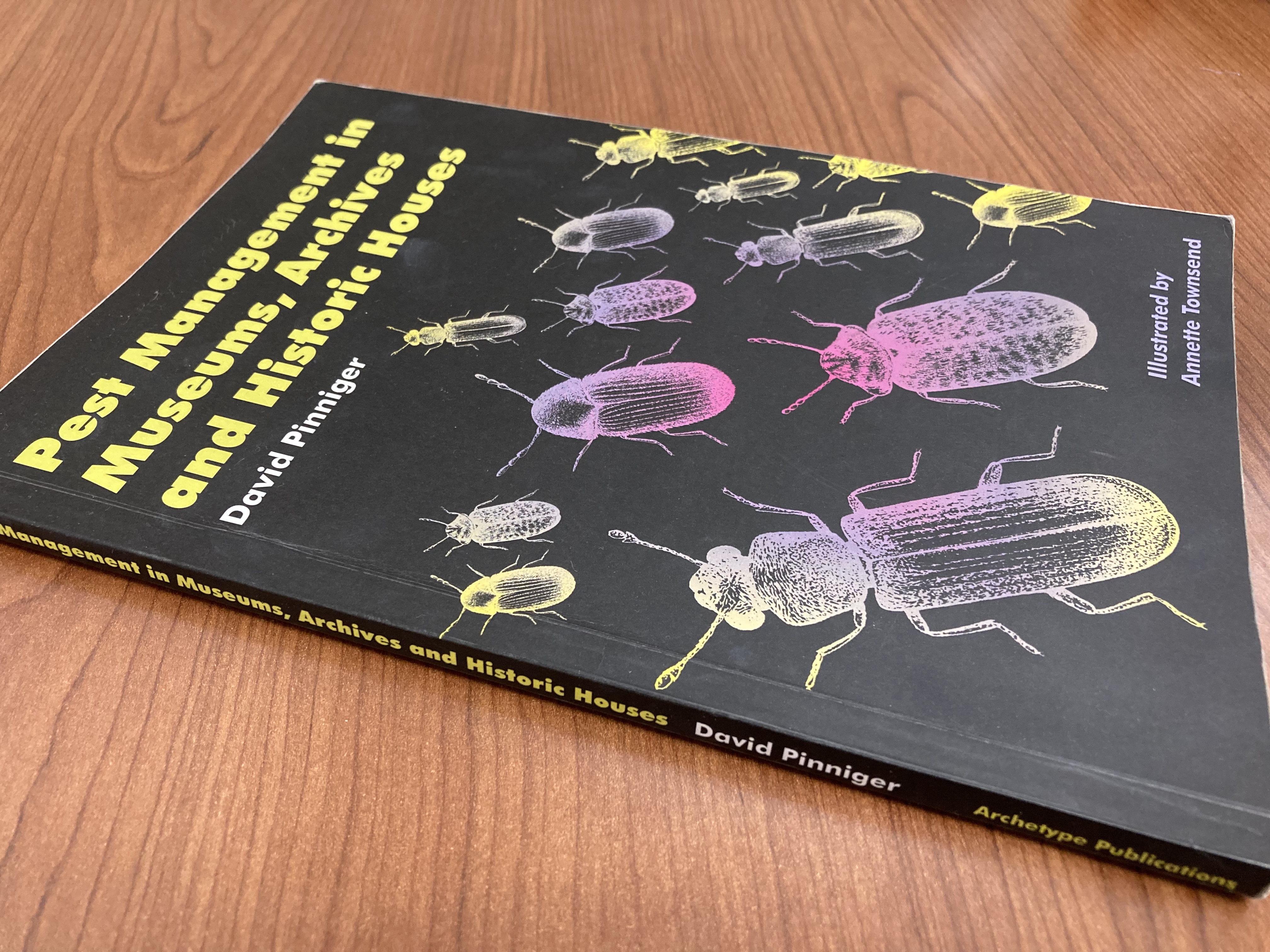 A book by David Pinniger titled, “Pest Management in Museums, Archives and Historic Houses.” The book is a black paperback with yellow and white lettering and drawings of beetles on the cover. 
