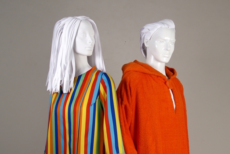 Two white mannequins wear a loose rainbow robe and a red fuzzy robe.