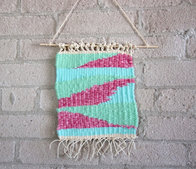 A pastel coloured tapestry wall hanging, hanging against a white brick wall