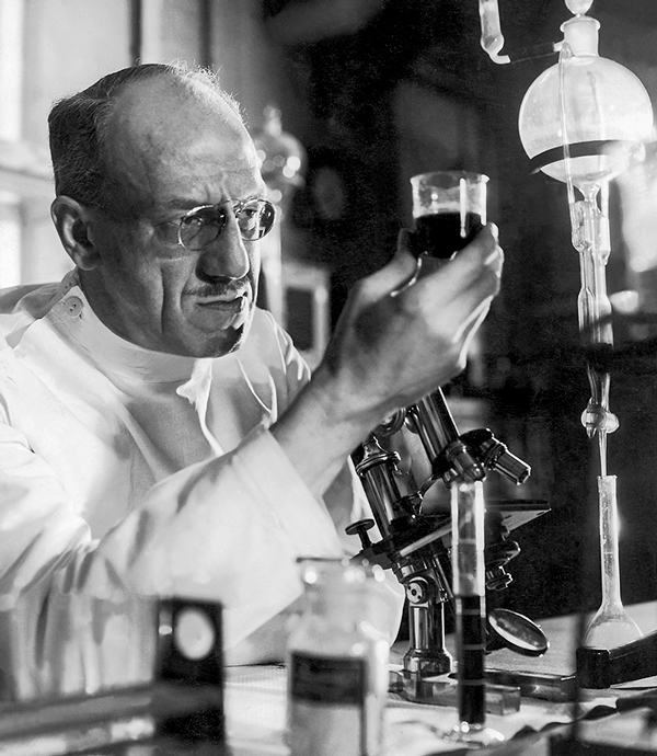 Archival photo of a mature male scientist looking pensively at a vial of liquid in his laboratory
