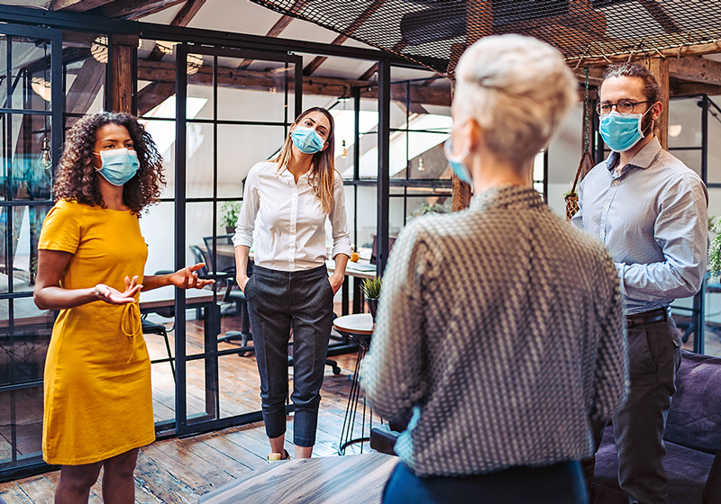 Photo of a group of people talking in an open office, all are wearing protective masks