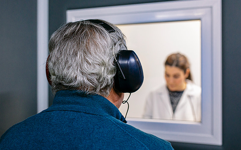 Mature male adult with headphones on, taking a hearing test in a soundproof booth