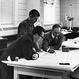 Black-and-white archival photo of three researchers at a lab table undertaking seismological investigations in 1962. 
