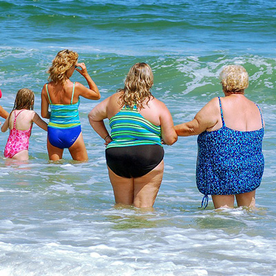 People of all sizes at a beach standing in the water in swimsuits.