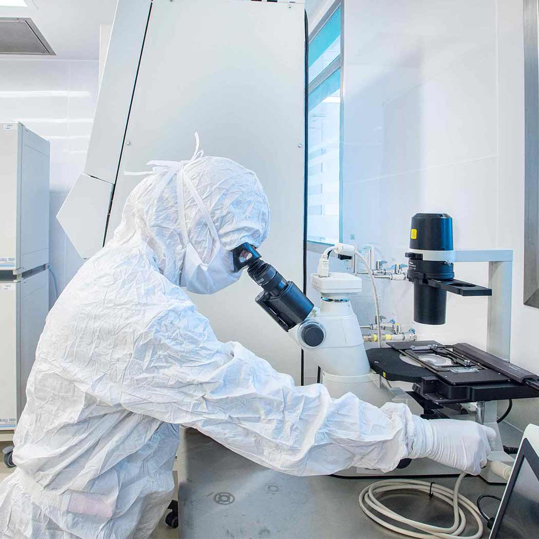A researcher in a clean suit looks into a microscope