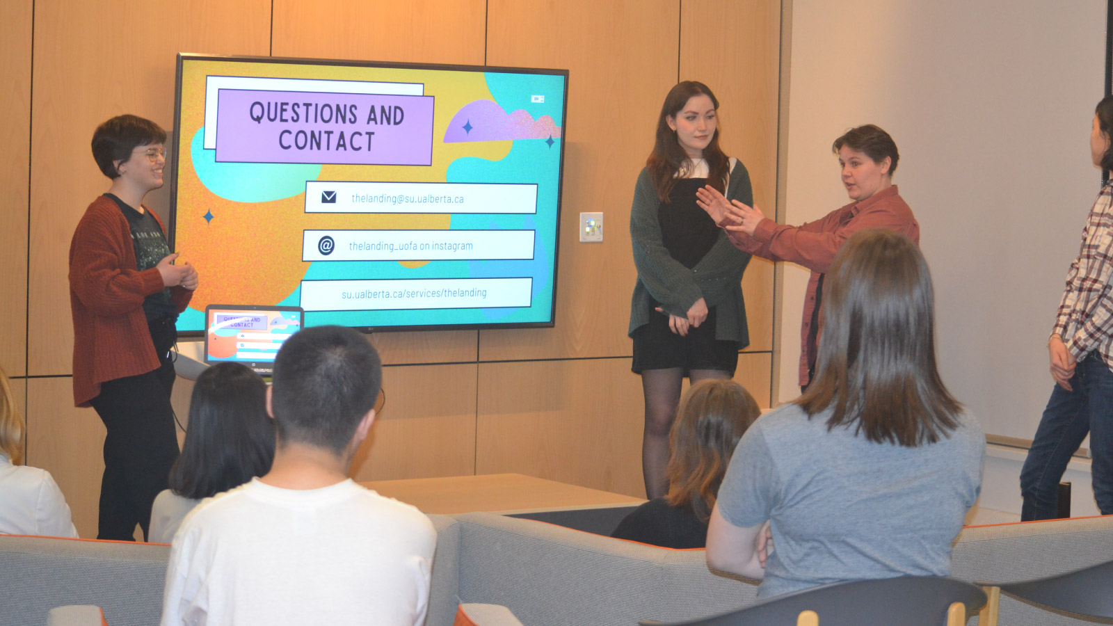 Presenters stand in front of a group of students with a question and contact slide behind them.