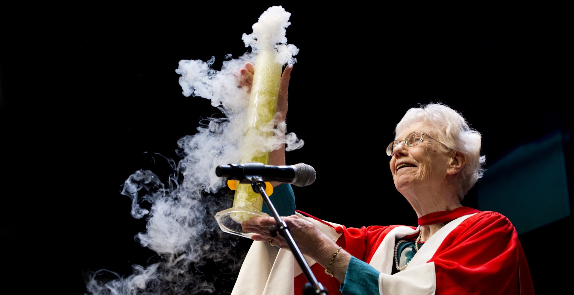 Margaret-Ann Armour during her Convocation address, holding aloft a tall beaker with plumes of gas leaking out