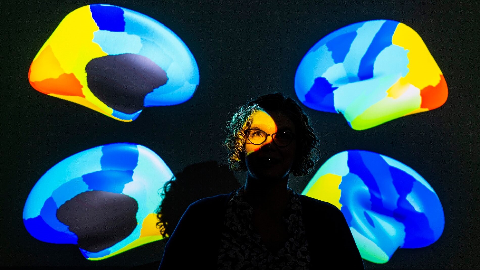 Alona Fyshe standing in front of a projection of 4 brain scans, with a text overlay reading Artificial Intelligence at UAlberta