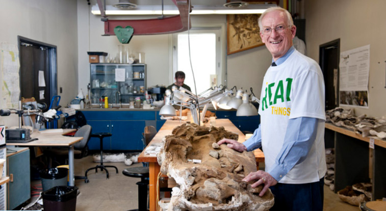 Volunteer Preparator of dinosaur remains, Christopher Harrison cleaning fossils at a table in the Dino Lab.