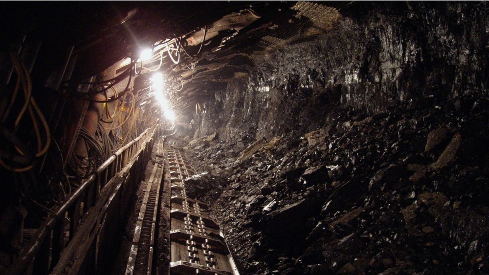 a tunnel inside a coal mine with tracks and machines, with light in the distance