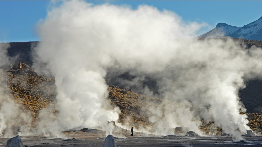 Clouds of steam billowing from geysers in front of a range of hills