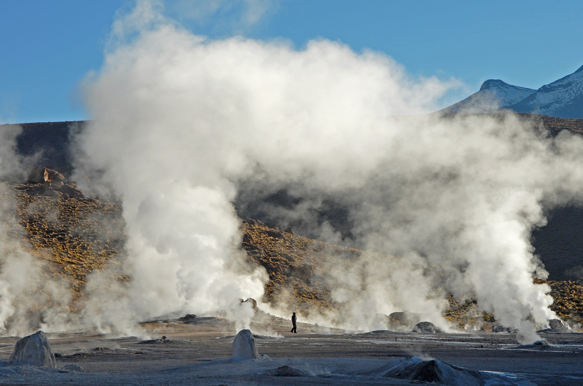 Clouds of steam billowing from geysers in front of a range of hills