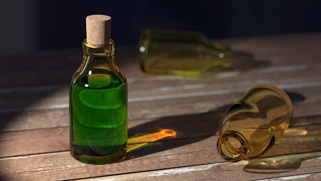 Corked bottle of green liquid standing on hardwood floor, two empty bottles lay next to it.