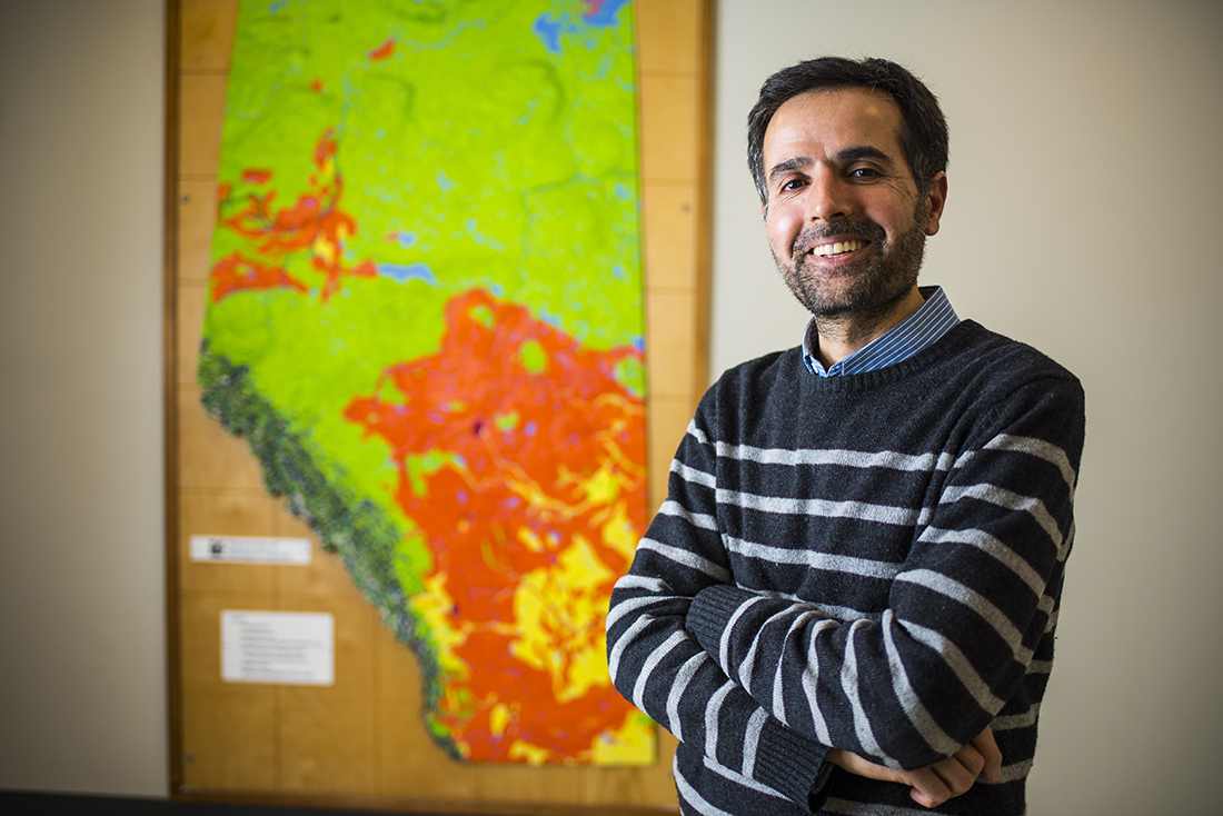 Computing Science Professor Davood Rafiei stands in front of a topographical map of Alberta, Canada.