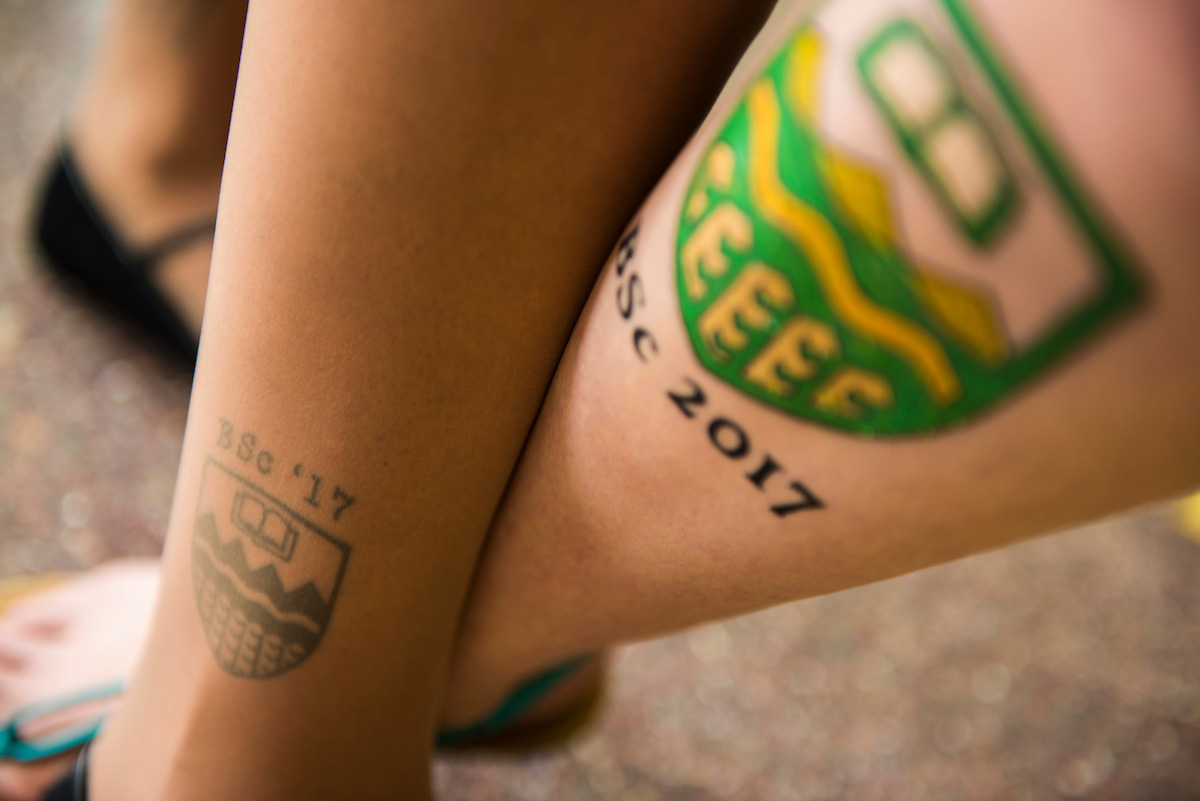 New bachelor of science graduate Brooke Biddlecombe gets the UAlberta insignia inked on her leg.