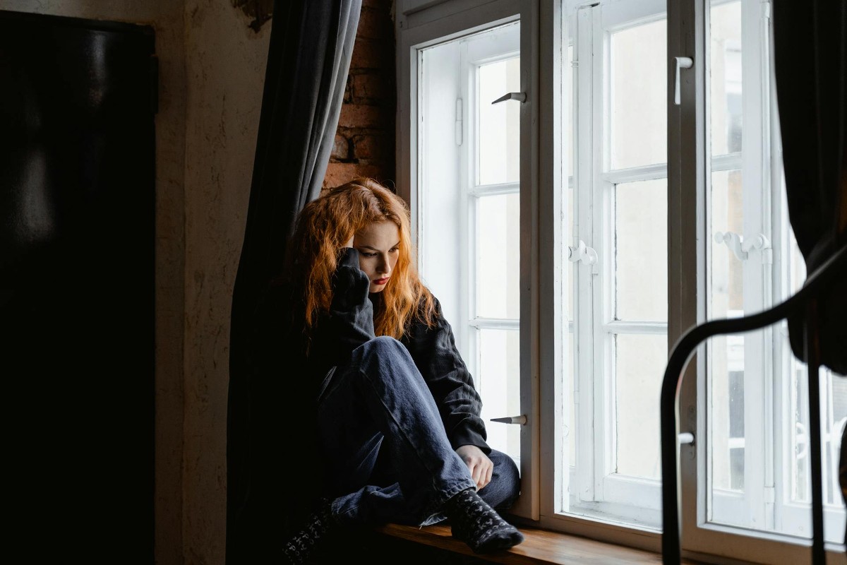 A woman sits near a window in a darkened room, looking deep in thought. In this issue of Dear Maddi, psychologist and guest author Dr. Brittany Budzan discusses why change can feel so hard even when we know we need it.