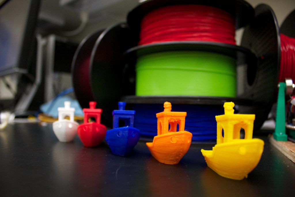 White, red, blue, orange, and yellow 3D printed tugboats in a row
