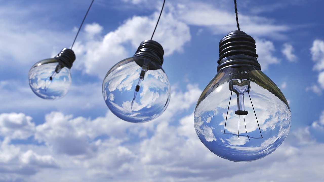 three incandescent light bulbs suspended in the air, blue skies in the background
