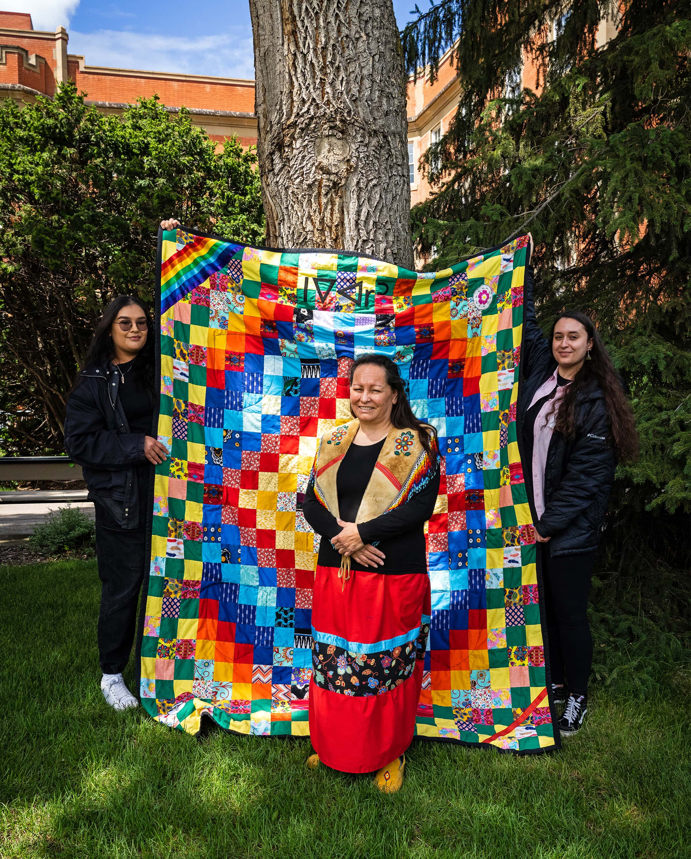 Elder Heather Poitras stands with the ceremonial quilt made for the ISP, held by her daughters.