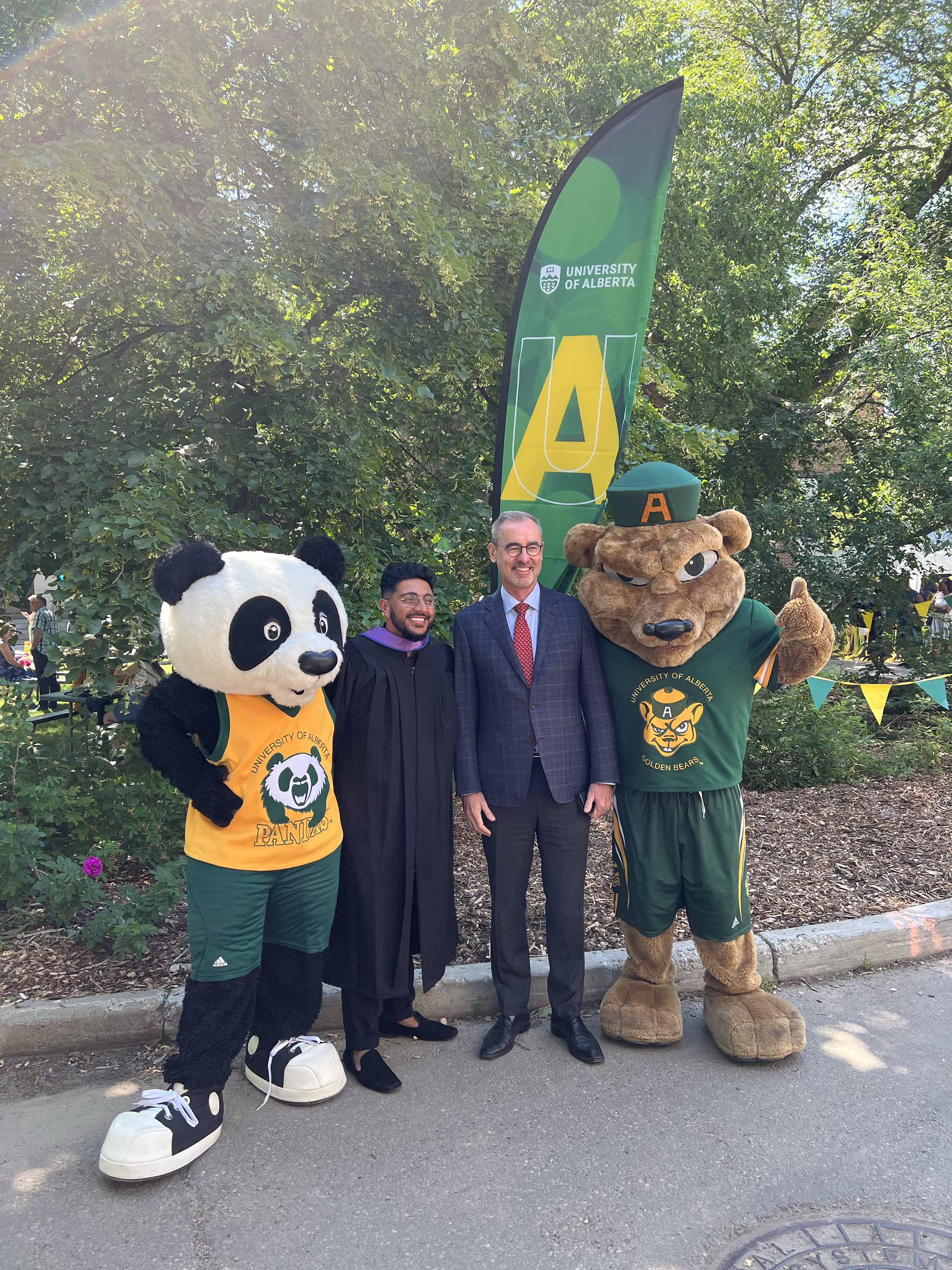 A grad poses with President Flanagan, Patches and Guba.