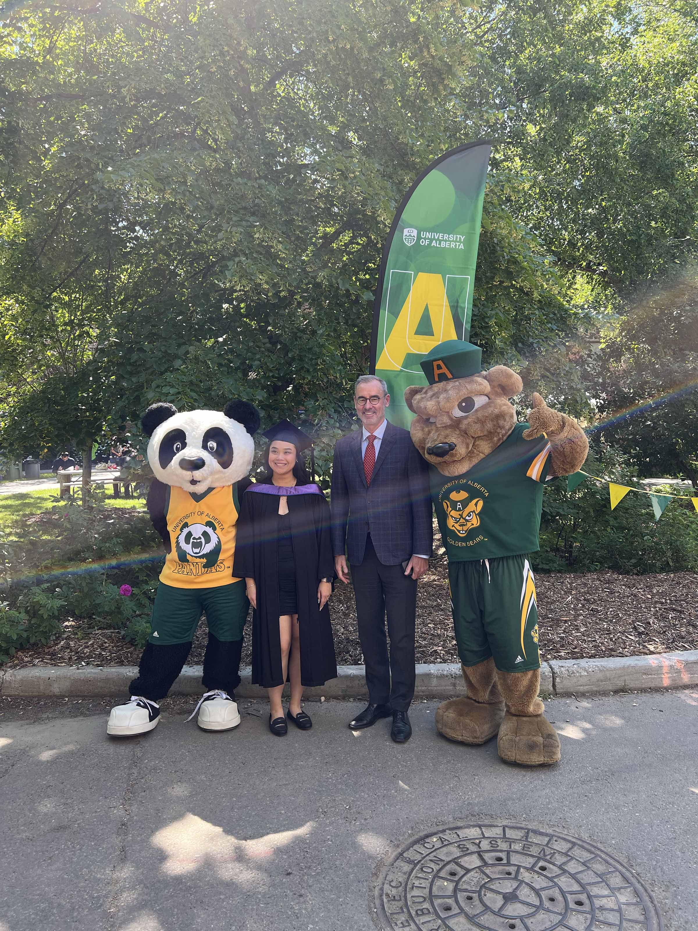 A graduate poses with President Flanagan, Patches and Guba.